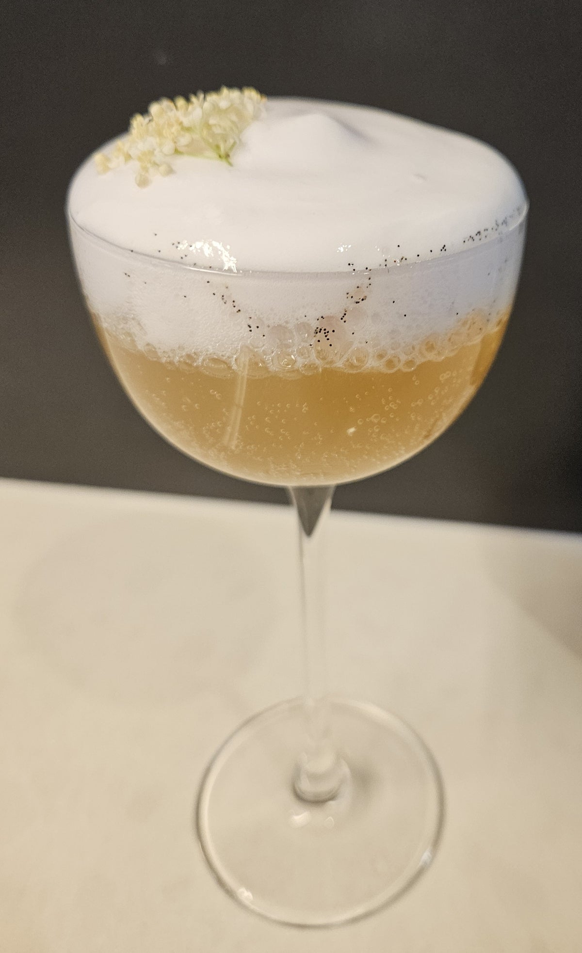 A foamy Better Brew drink in a coupe glass with a small flower garnish.