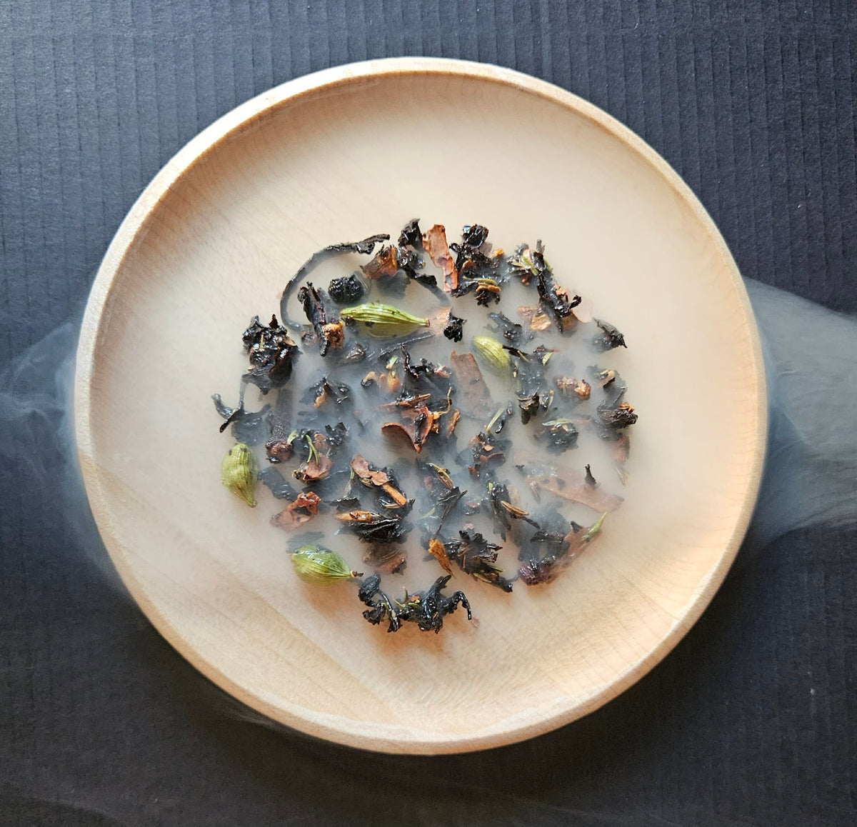 Smoked Tartufo Wet Chai with whole spices in a wooden bowl on a dark surface.